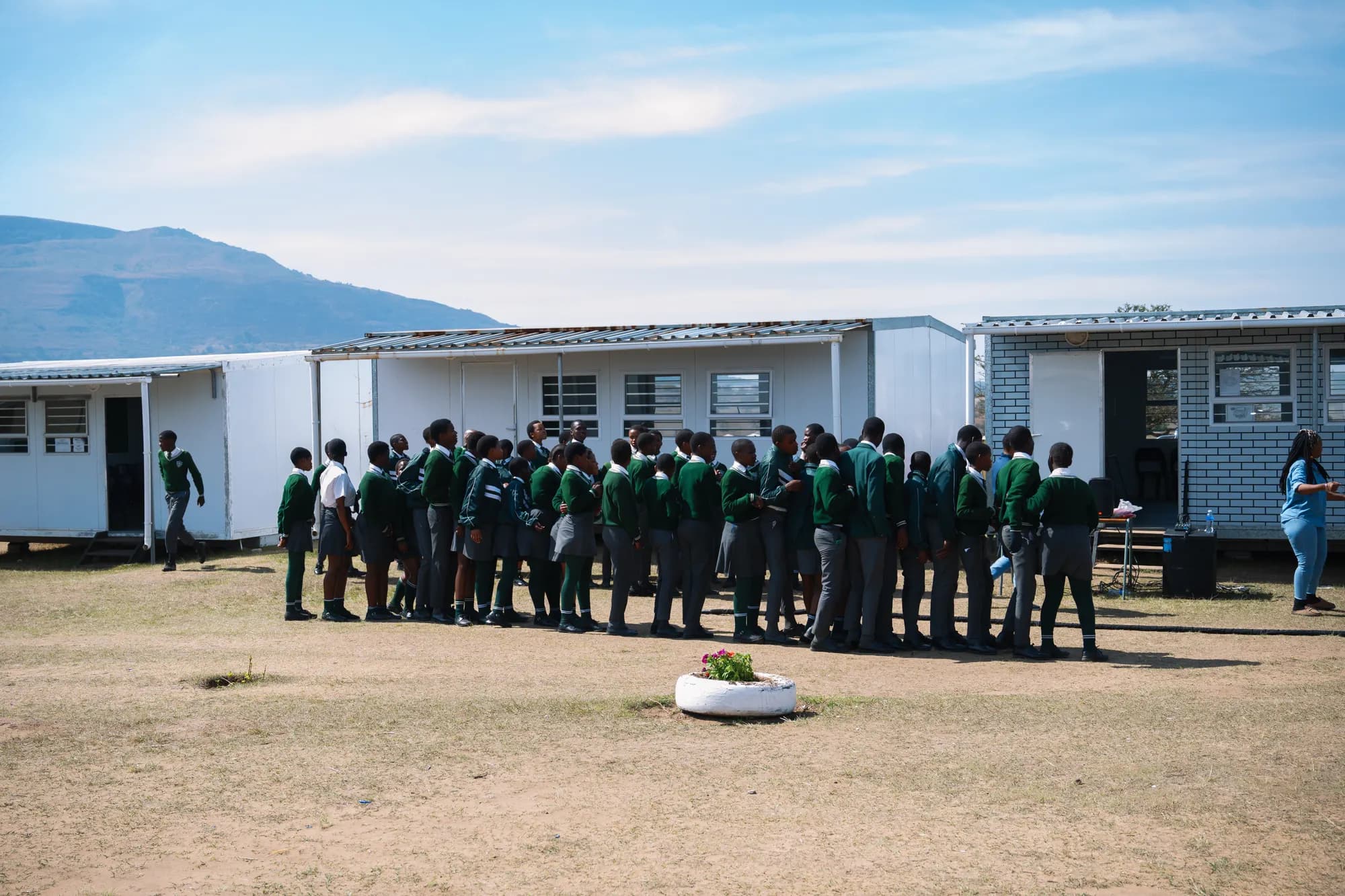Learners in green blazers gathered outside classroom blocks at a Phakamani school session